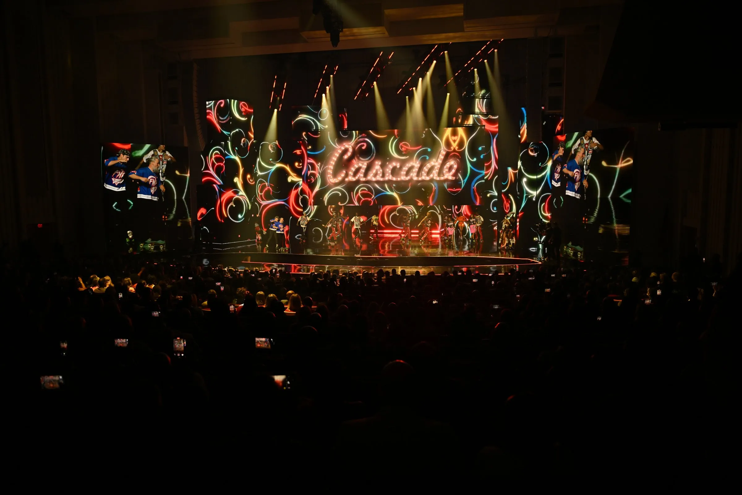 Beloved Benefit Cascade performance — "Cascade" cursive marquee on the main LED with neon scrollwork backdrop, side IMAG screens, dancers on stage and packed audience visible