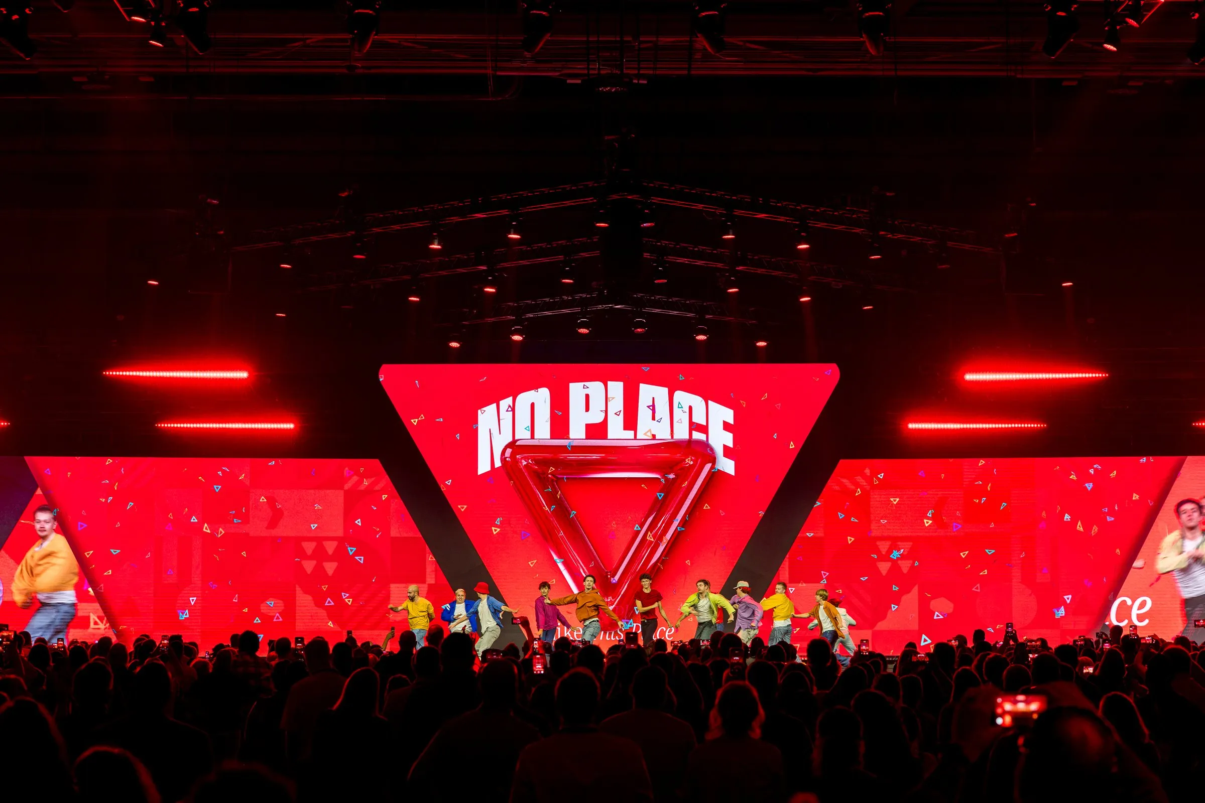 Dance performance in front of a red 'No Place' look with a glossy 3D Y triangle and patterned wings