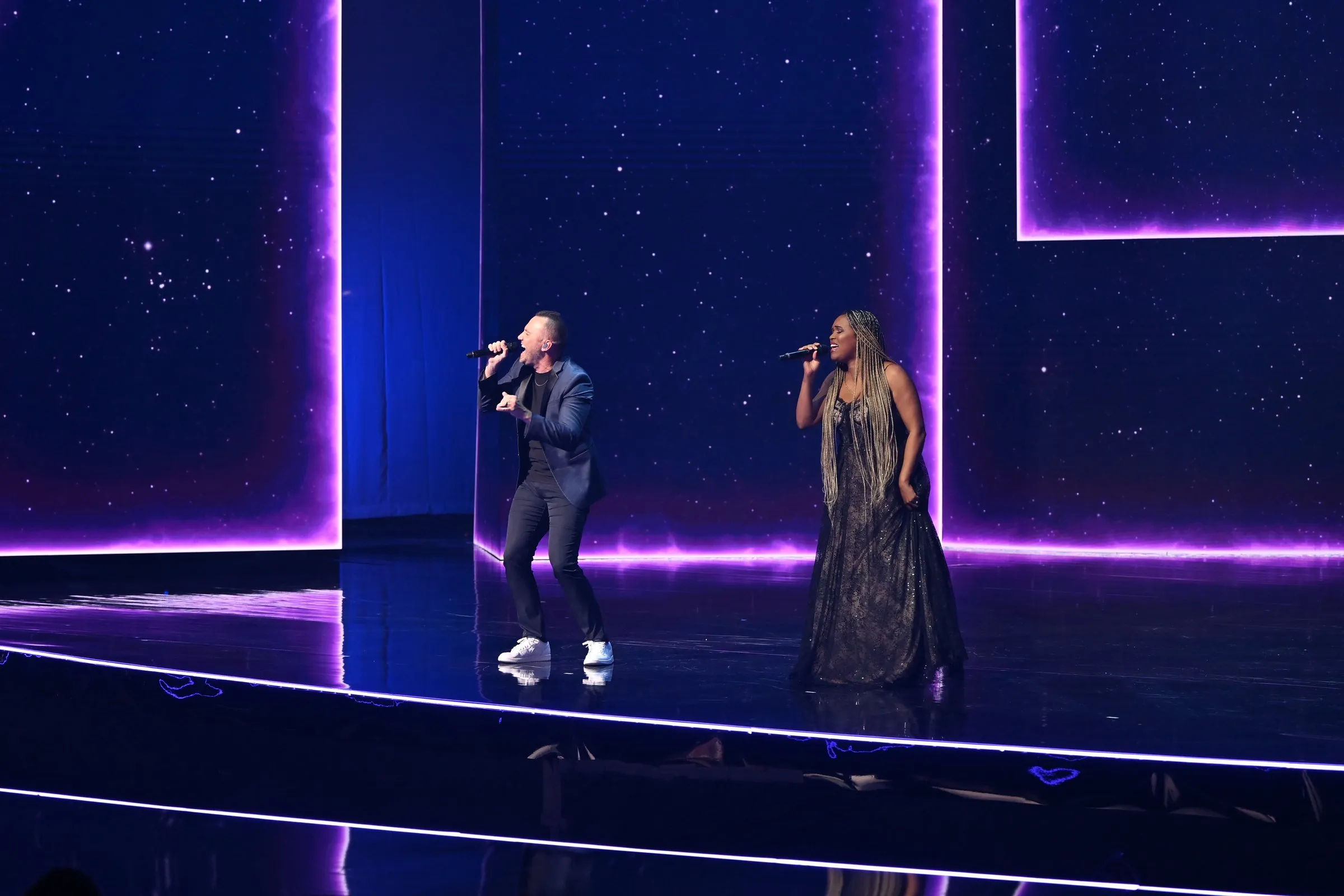 Beloved Benefit duet — two vocalists on stage in front of a starfield backdrop framed by neon-pink rectangular light frames