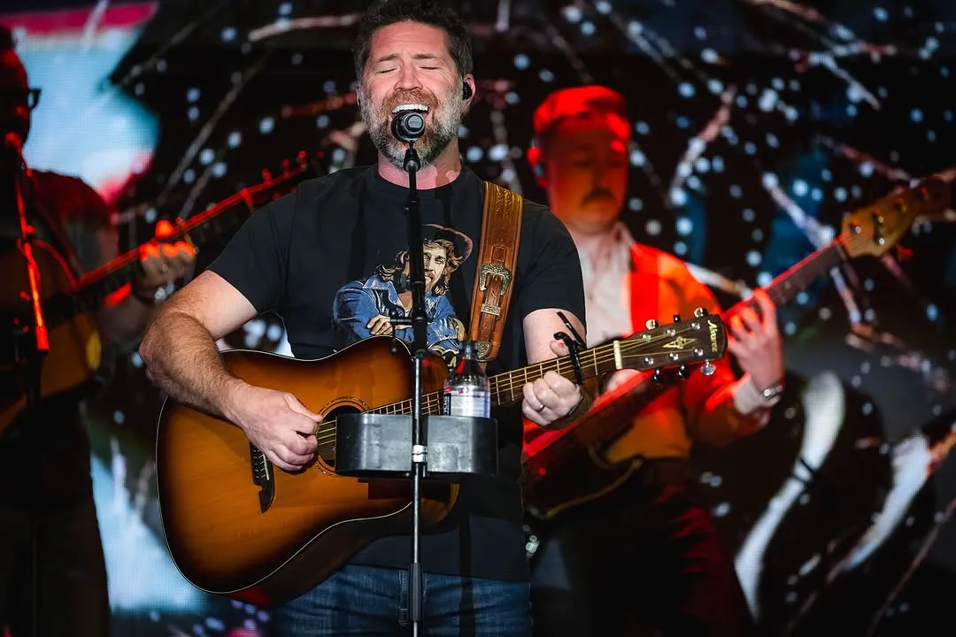 Josh Turner singing into the microphone with acoustic guitar, starlight pattern on the LED behind him