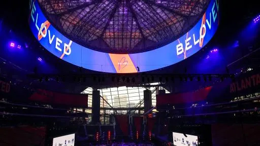 Beloved Benefit at Mercedes-Benz Stadium — the stadium's petal roof carrying the BELOVED wordmark in projected light, audience filling the bowl below