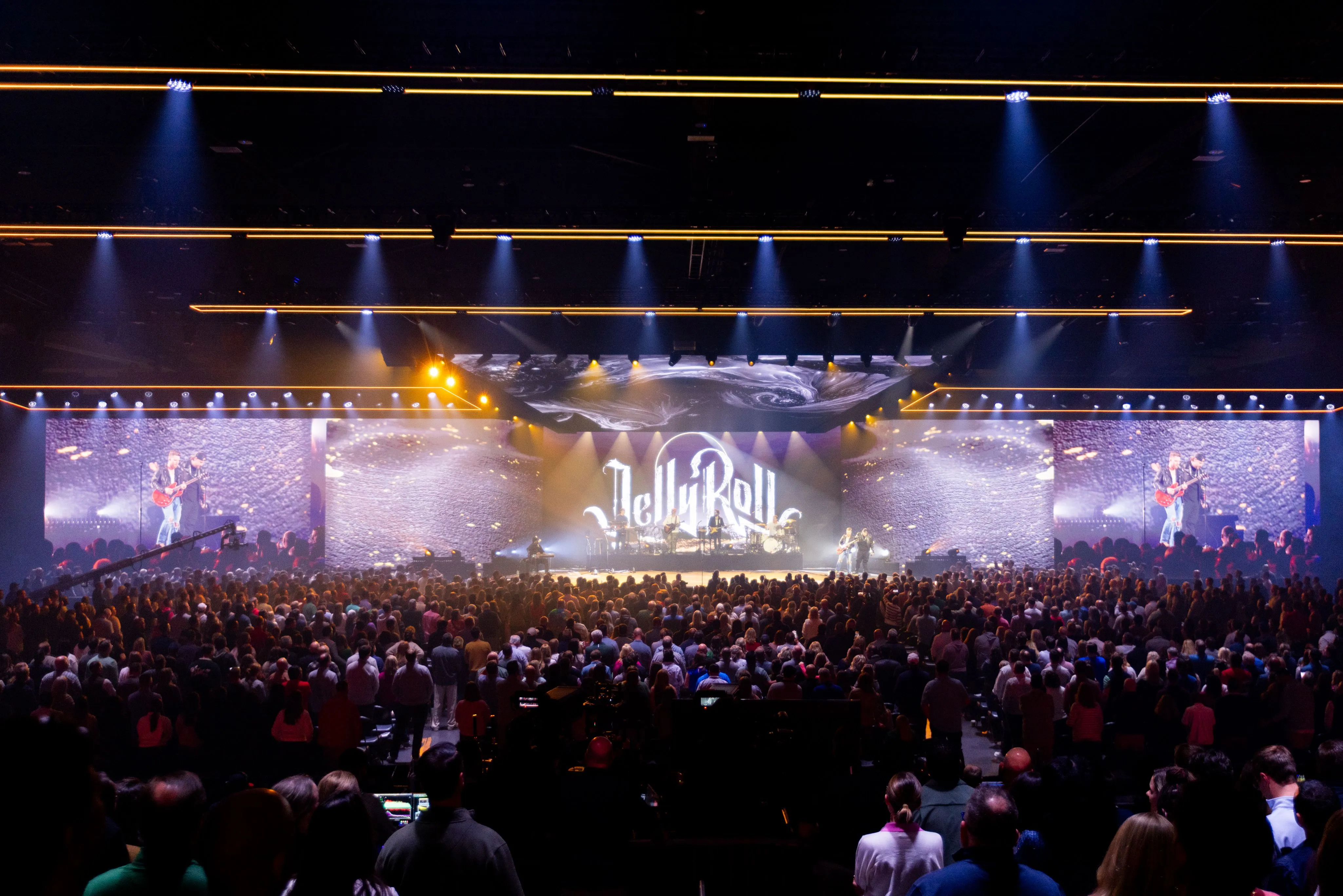 Musical artist support — Jelly Roll on a wide arena stage with stone-textured LED backdrop and side IMAG screens