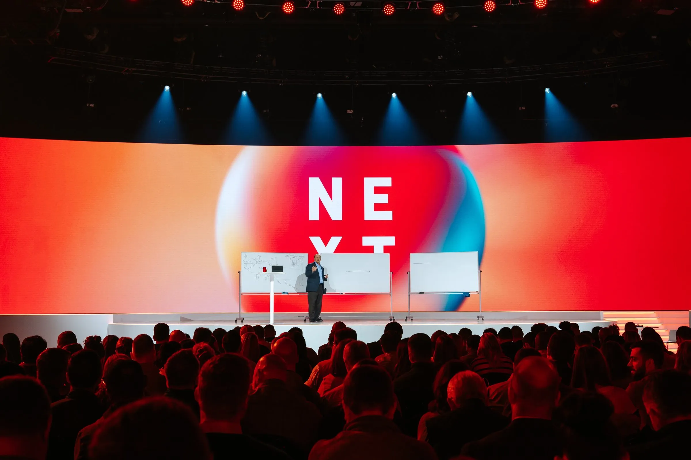 NEXT 2023 stage — "NEXT" wordmark over a sunset gradient backdrop on a wide curved LED wall
