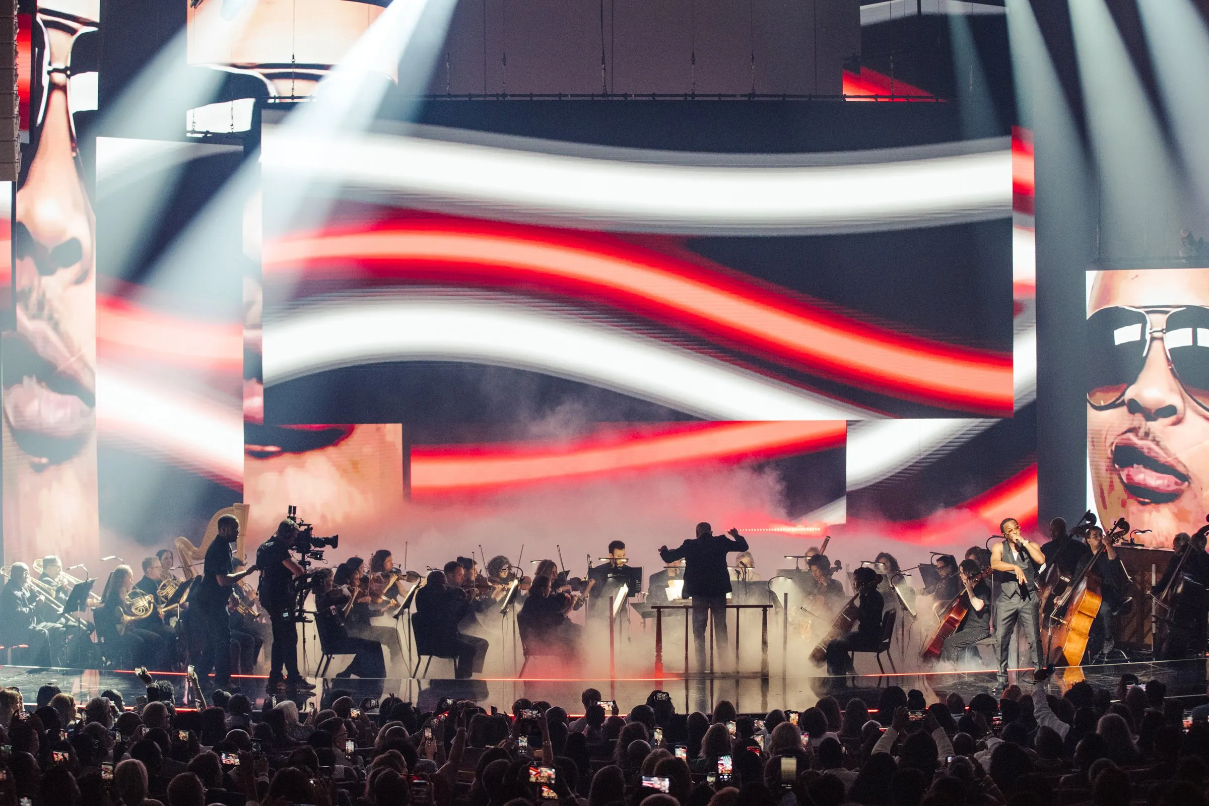 Beloved Benefit orchestra performance with a striped wave-like LED treatment across the back wall and side IMAG showing performer portraits