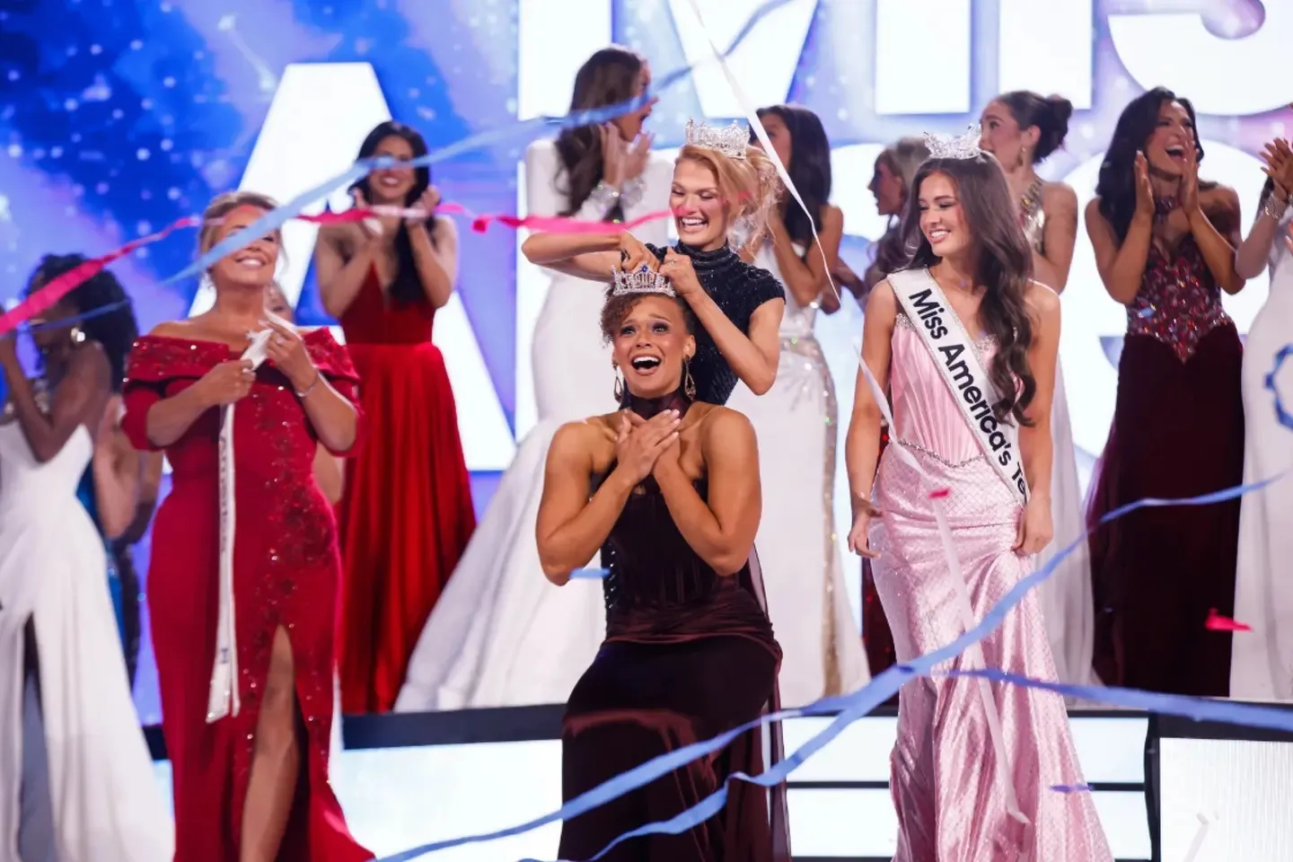 The crowning moment — the new Miss America reacts as the crown is placed, surrounded by contestants and streamers in front of the LED wall
