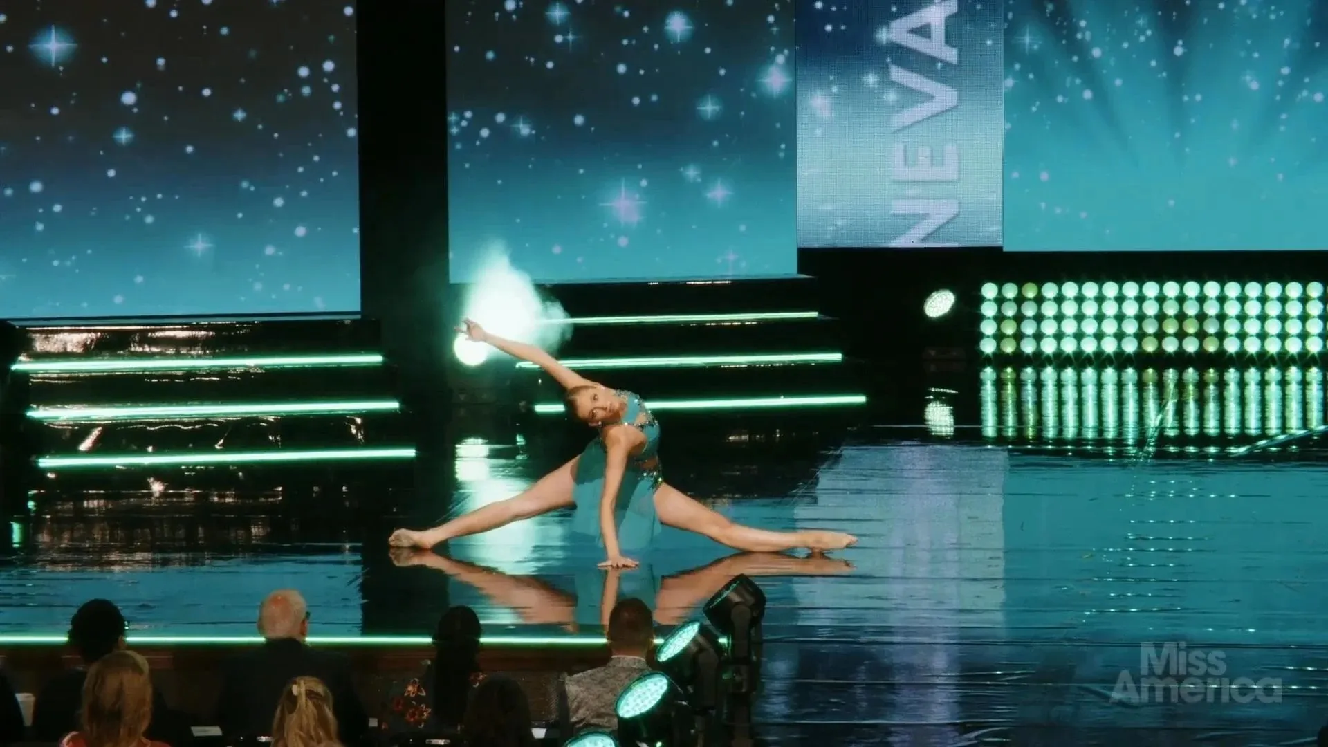 A talent performance — a dancer in teal on the reflective stage floor in front of starfield LED content and a state-name graphic