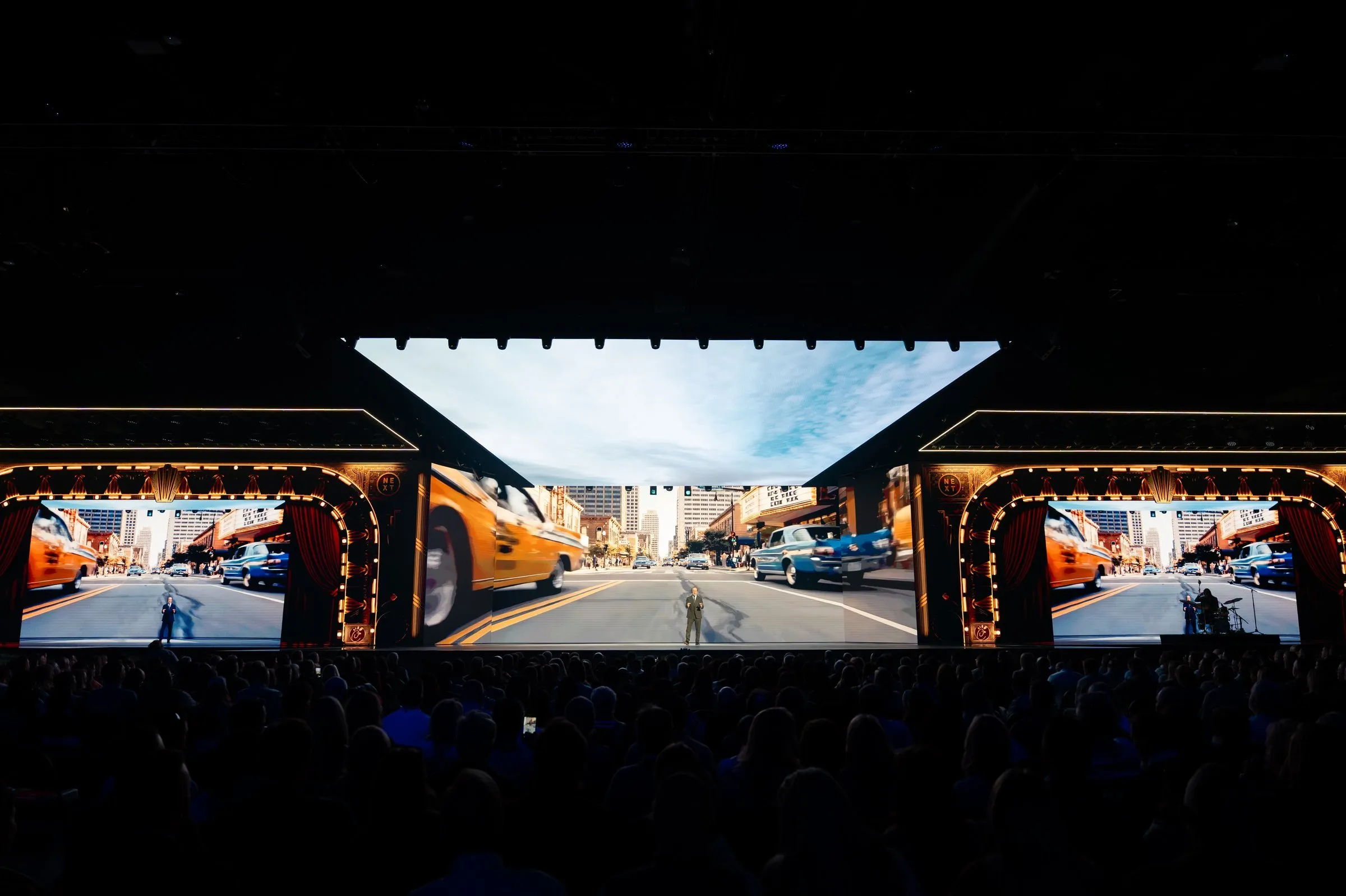 NEXT 2026 — three-screen panoramic theater storyline with a vintage marquee proscenium framing a city-street scene